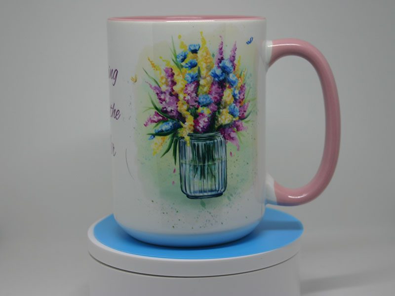 A mug with flowers on it sitting on top of a coaster.