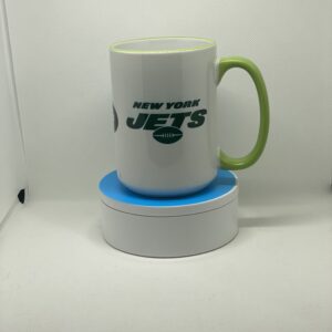 A white and green mug sitting on top of a blue coaster.