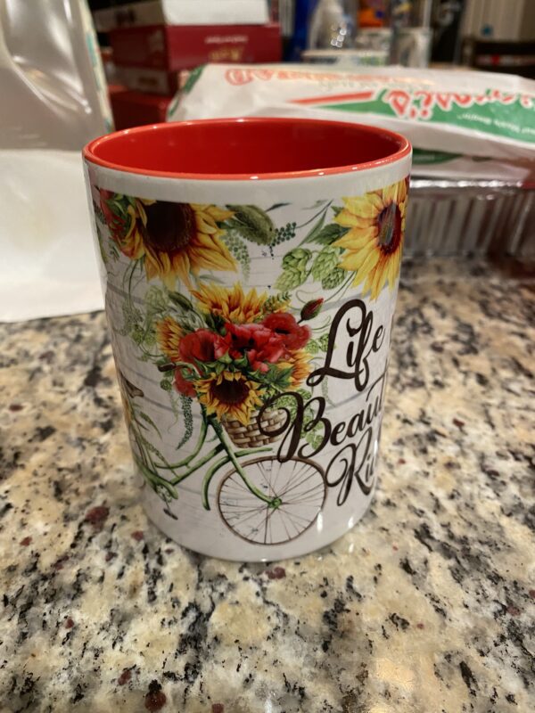 A coffee mug with sunflowers and the words " life is beautiful ".