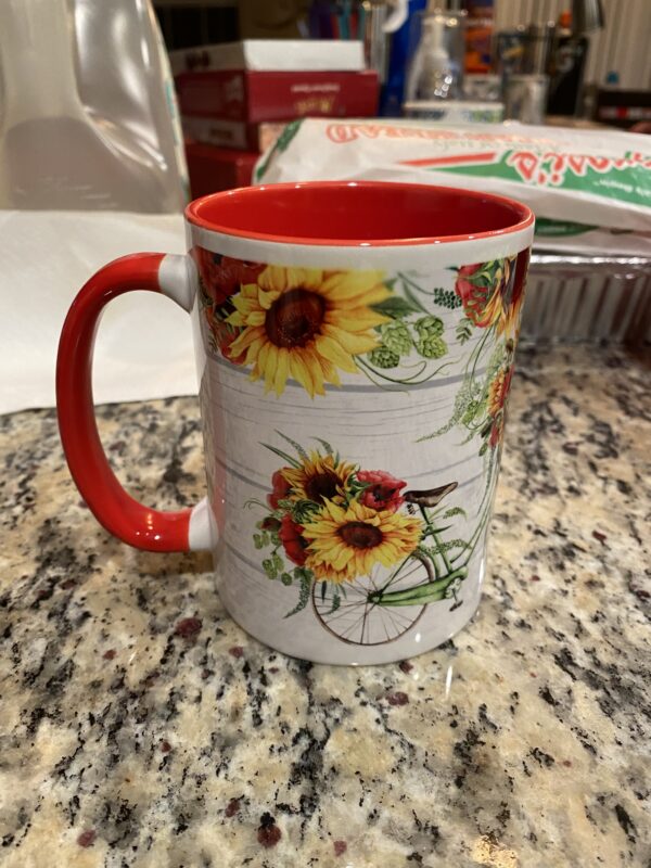 A coffee mug with sunflowers on it sitting on top of a counter.