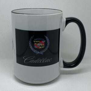 A white coffee mug with black rim and a cadillac logo on the side.