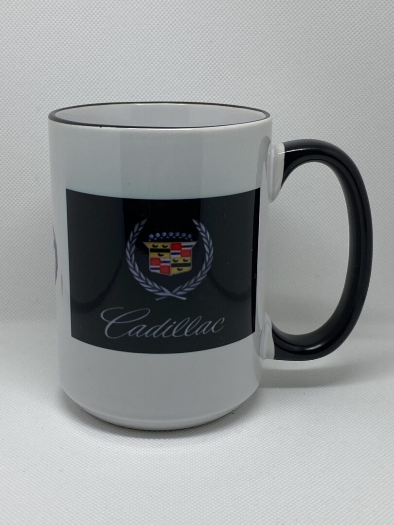 A white coffee mug with black rim and a cadillac logo on the side.