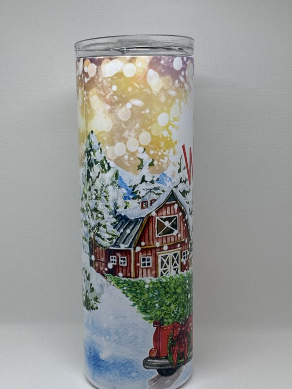 A candle with a painting of a house and trees.