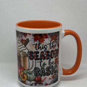A coffee mug with an orange handle and the words " this is the season to be basic ".