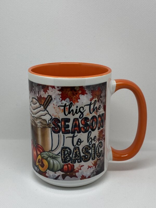 A coffee mug with an orange handle and the words " this is the season to be basic ".