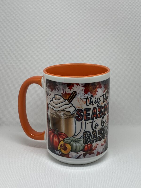 A coffee mug with an orange handle and the words " this is the season to be baked ".