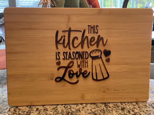 A cutting board with the words " this kitchen is seasoned with love ".