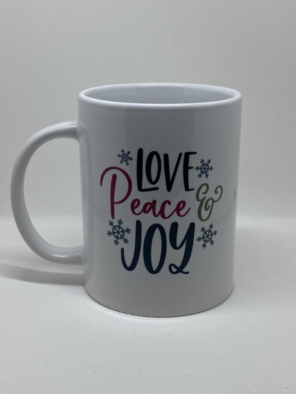 A white coffee mug with the words love peace and joy written on it.