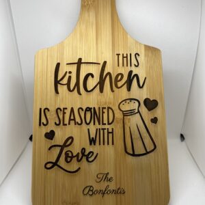 A wooden cutting board with the words " this kitchen is seasoned with love ".