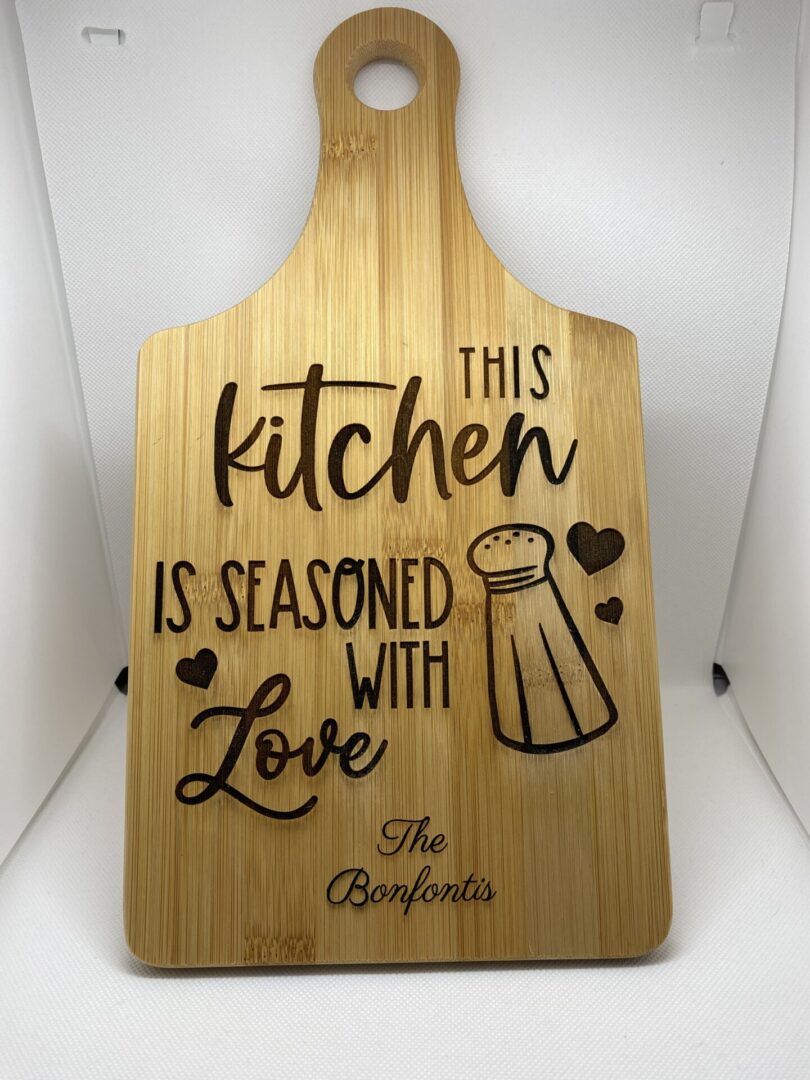 A wooden cutting board with the words " this kitchen is seasoned with love ".