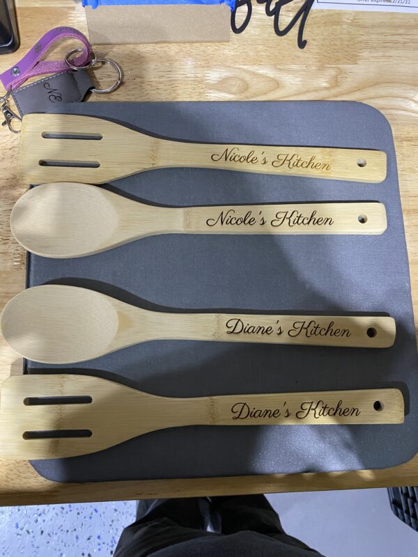 A wooden spoon and fork set with the name nicole 's kitchen engraved on it.